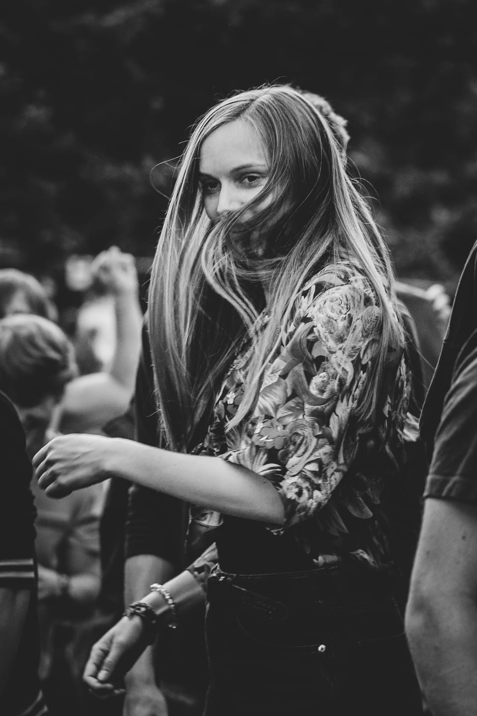 Junge Frau im Festivalpublikum blickt in die Kamera, ihr langes Haar weht quer über das Gesicht, Schwarzweiß.